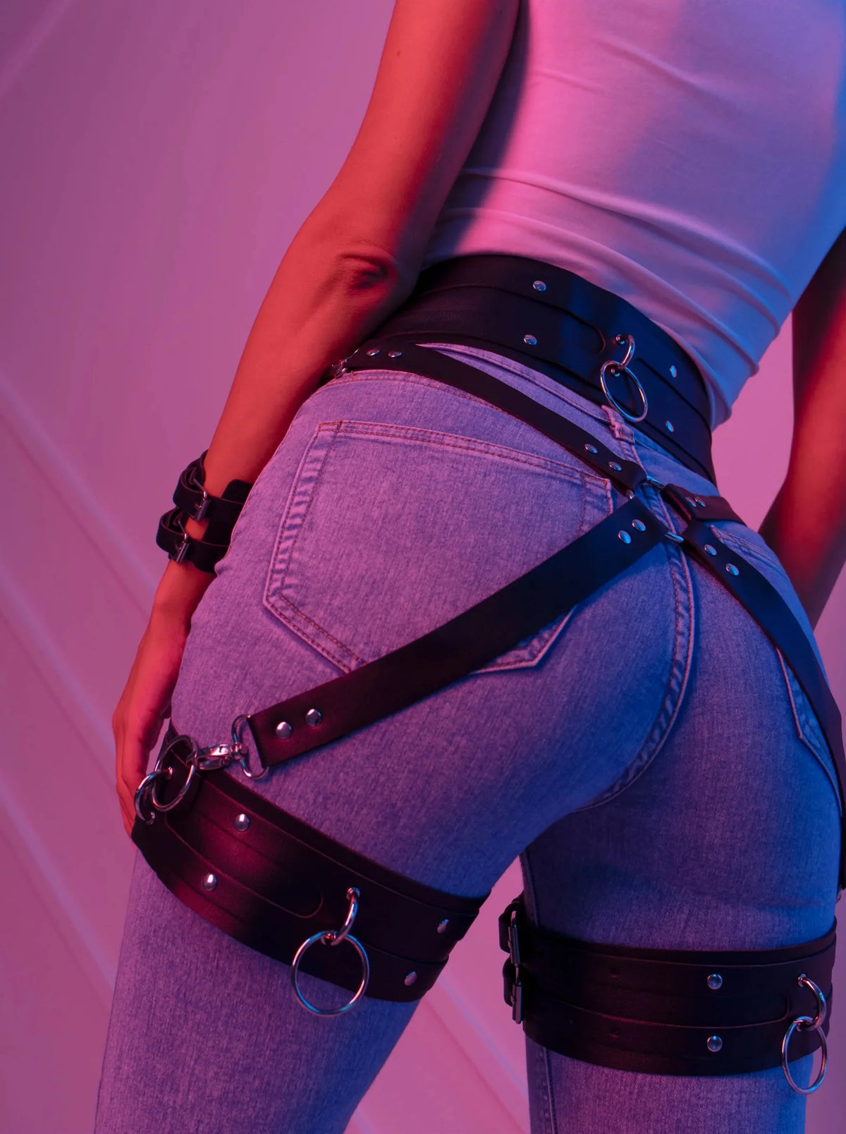 Black faux leather waist-to-thigh harness belt close-up with studded straps and O-rings
