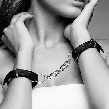 Black leather wrist cuffs with metallic chain worn on wrists